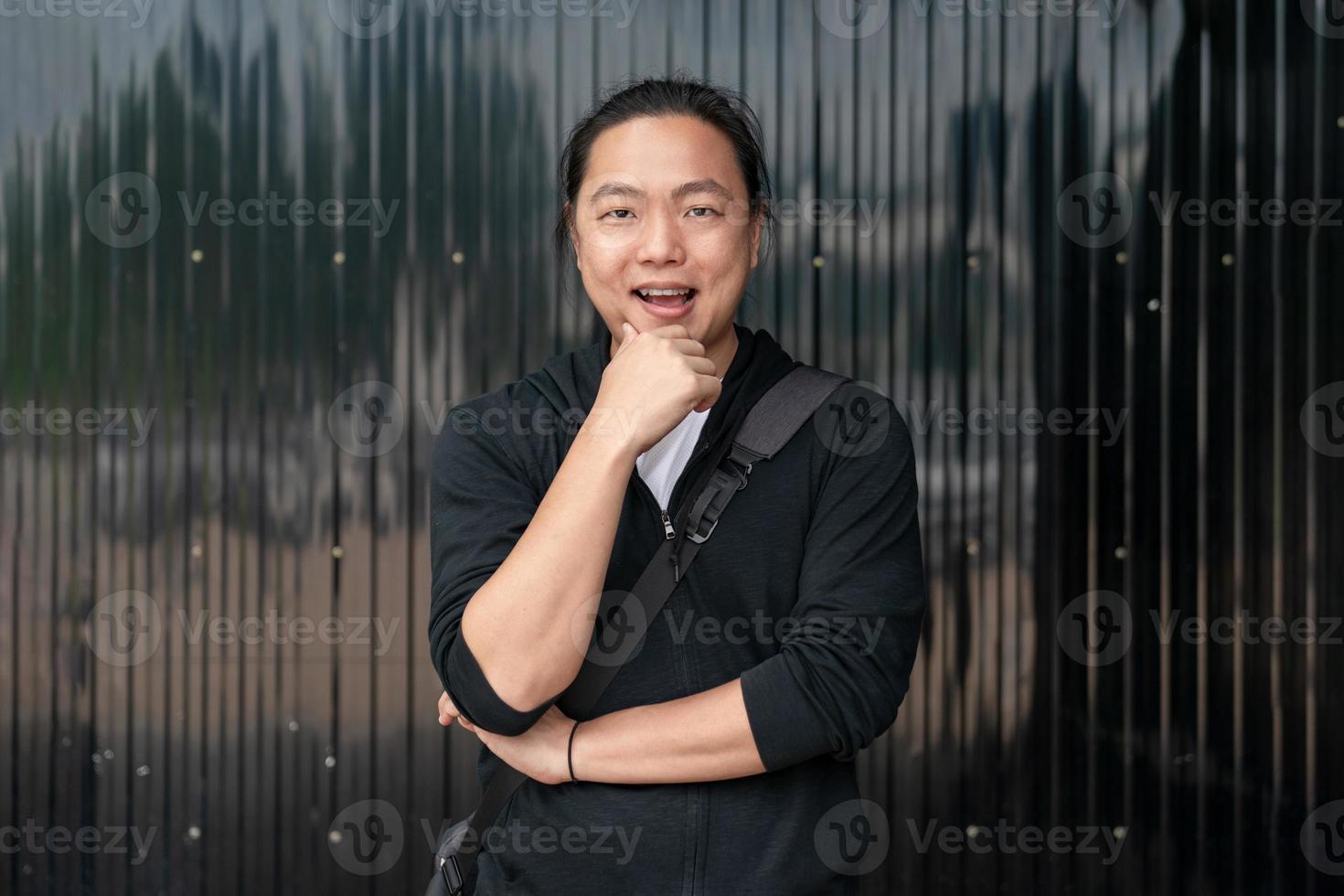 un homme asiatique se tient devant un fond de zinc noir avec une humeur confiante. photo