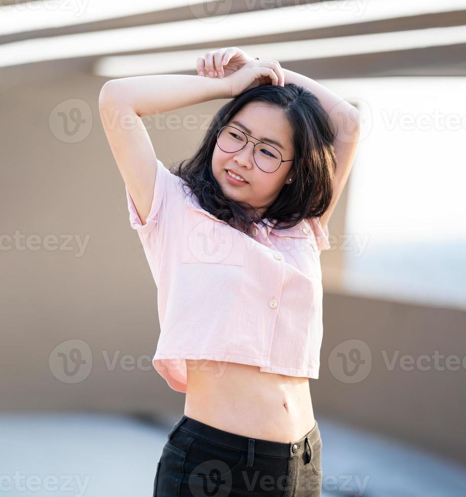 de belles lunettes femme asiatique lèvent la main et pose pour une image dans l'environnement extérieur du bâtiment sur le toit. photo