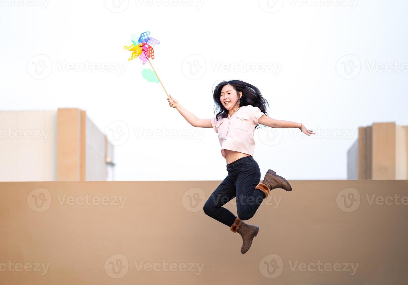 une femme asiatique poste, joue et saute avec un jouet moulin à vent couleur arc-en-ciel coloré sur le toit du bâtiment au coucher du soleil. photo