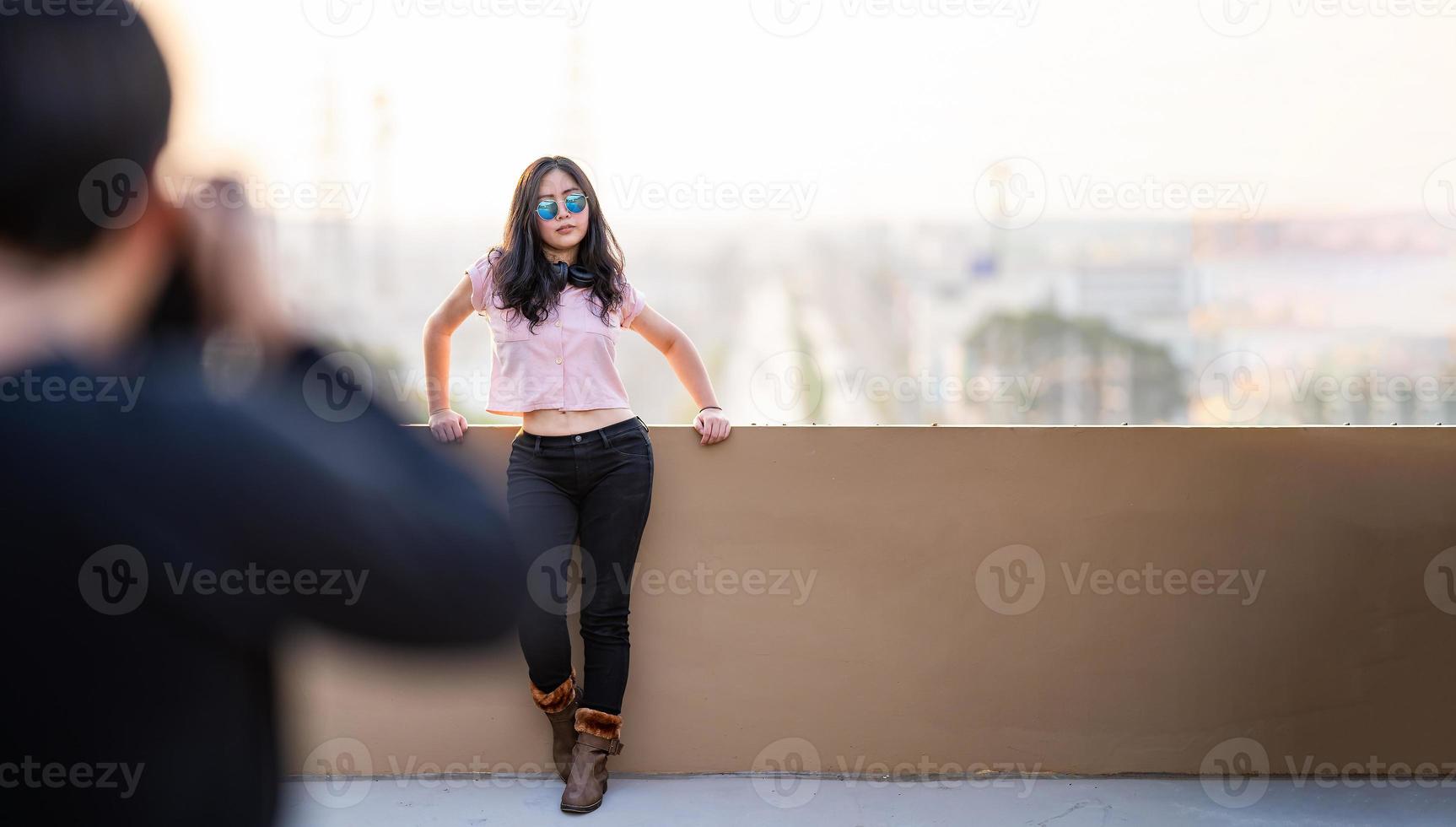 une femme modèle asiatique pose pour un photographe pour photographier un endroit sur le toit avec une vue floue sur la ville au crépuscule. photo