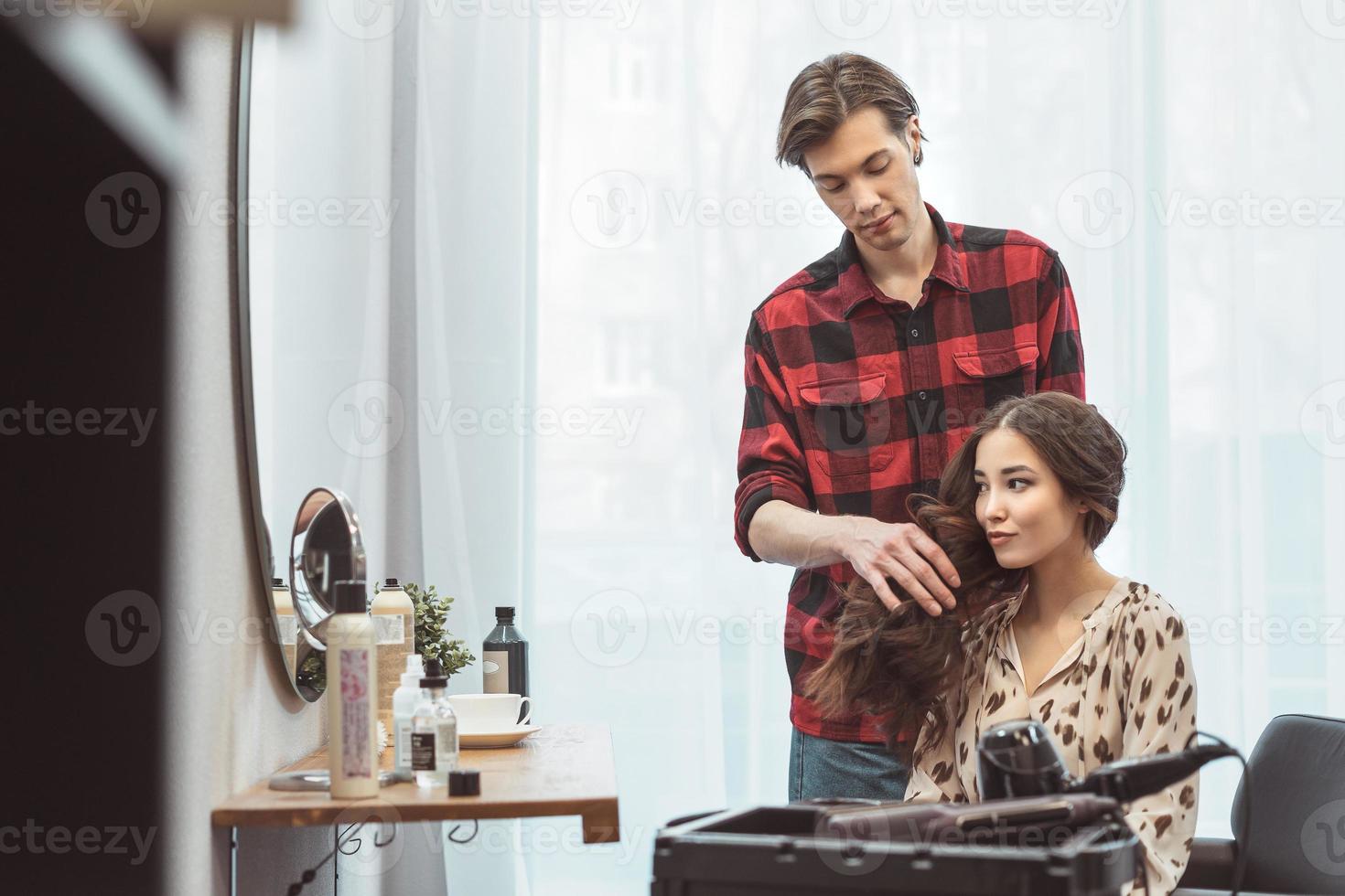 coiffeur styliste coiffant les cheveux longs pour une belle jeune femme asiatique dans le salon de beauté, moment de travail photo