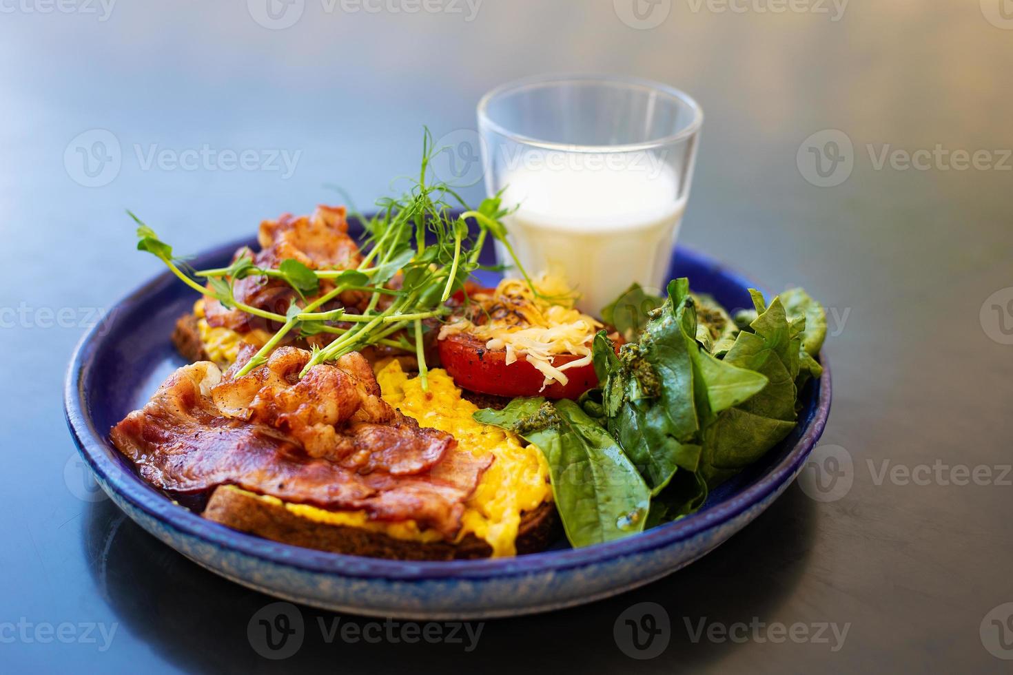 petit déjeuner très lumineux et sain sur une assiette - bacon, œuf, salade, tomate, fromage, un verre de yaourt. photo