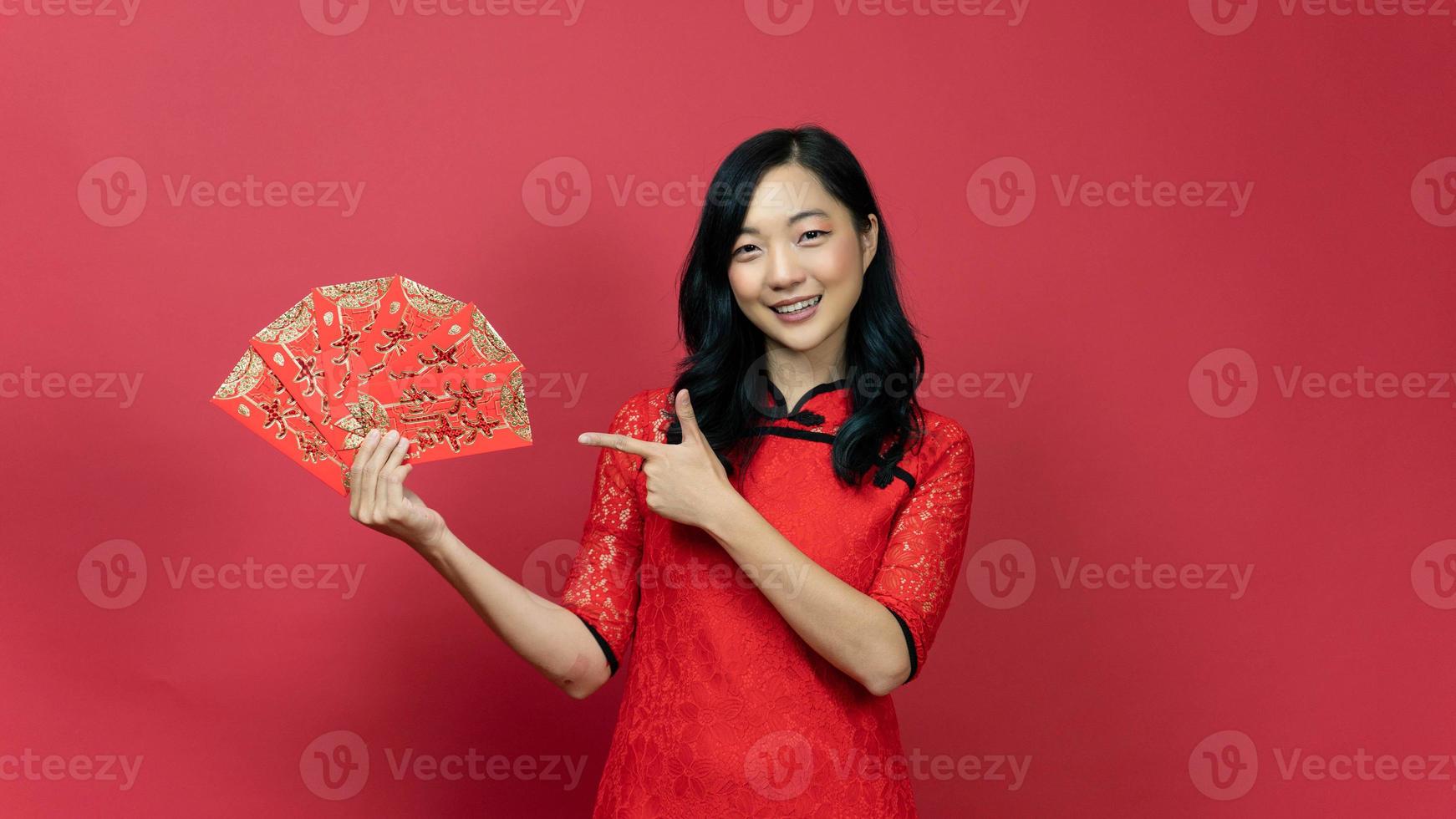 femme heureuse avec la main rouge cheongsam ou qipao pointant vers la carte de fortune de bénédiction isolée sur fond rouge. texte chinois signifie bonne chance grand profit photo