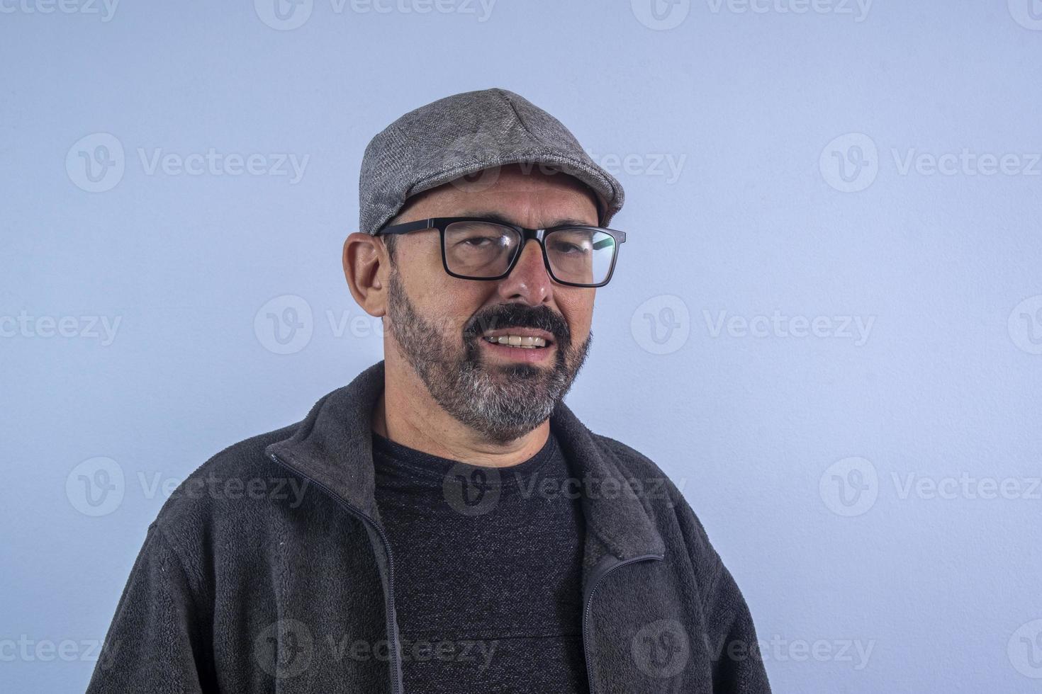 portrait d'homme barbu de 60 ans sur fond bleu avec chapeau et lunettes photo