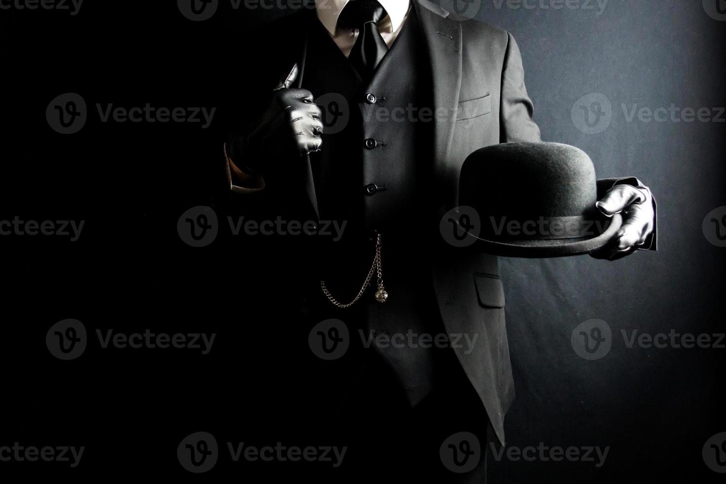 portrait d'homme en costume sombre et gants en cuir tenant un chapeau melon sur fond noir. concept de gentleman britannique classique photo