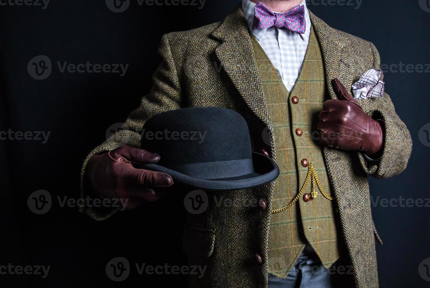 portrait d'homme en costume de tweed tenant un chapeau melon sur fond noir. style vintage et mode rétro du gentleman anglais. photo