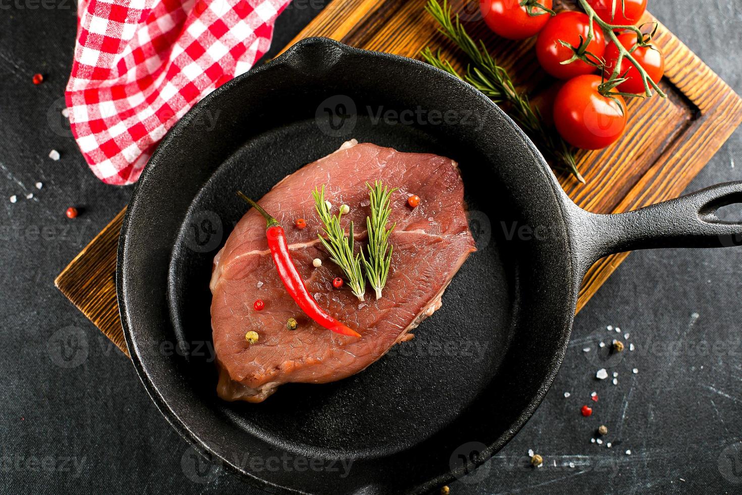 viande crue dans une poêle en fonte noire. steaks de porc aux épices, herbes fond sombre. vue de dessus photo