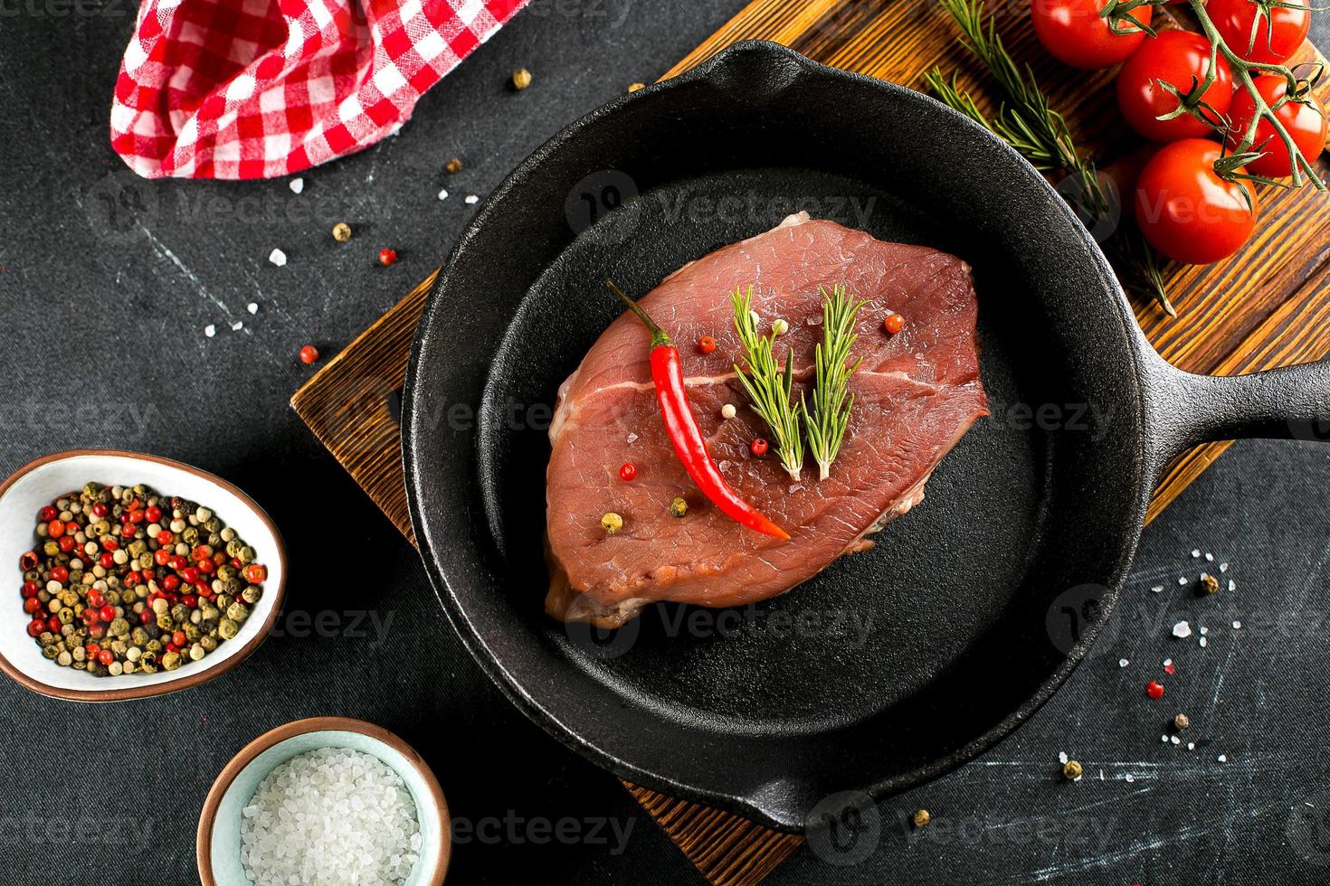 viande crue dans une poêle en fonte noire. steaks de porc aux épices, herbes fond sombre. vue de dessus photo