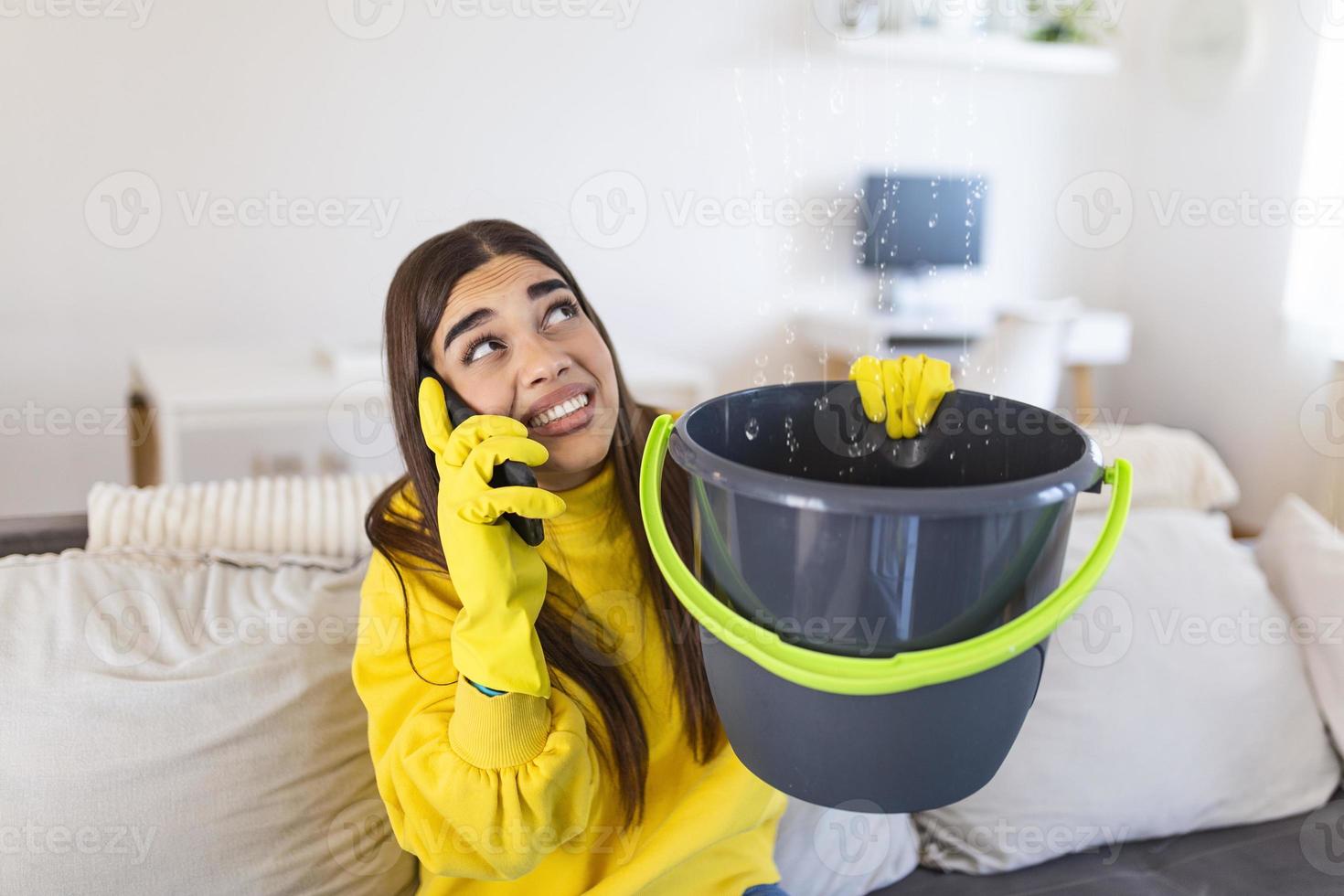 une jeune femme inquiète appelle un plombier pendant que l'eau de fuite tombe dans un seau à la maison photo