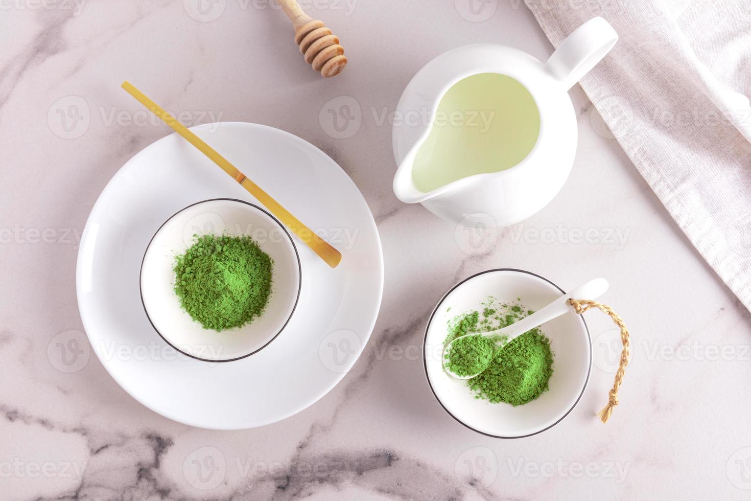 vue de dessus d'une table en marbre avec des bols de poudre de thé mat bio vert. un pot de lait pour faire un café au lait, une cuillère doseuse en bambou. photo