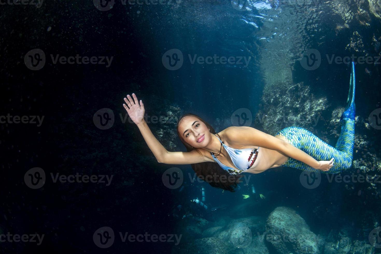 sirène nageant sous l'eau dans la mer d'un bleu profond avec des plongeurs photo