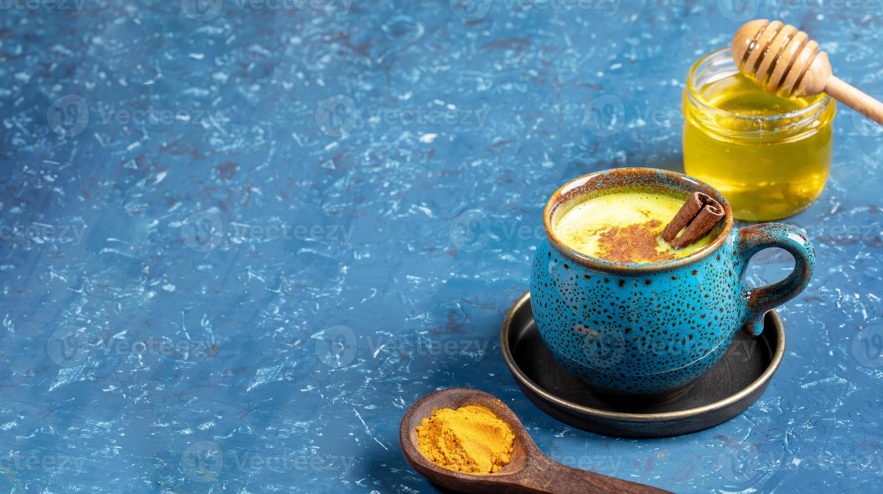 tasse de lait de curcuma doré, cuillère en bois avec poudre de curcuma et pot de miel sur bleu. mise au point sélective. espace de copie. photo