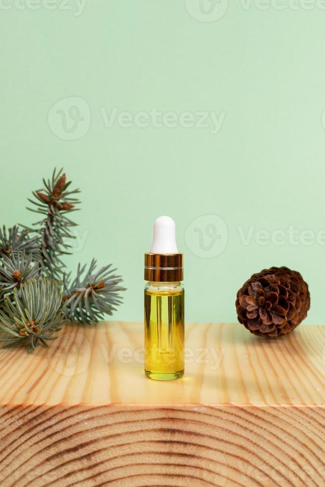 concept d'aromathérapie et de spa avec de l'huile essentielle d'épinette dans une petite bouteille en verre, brindille, cône sur support en bois sur vert. photo