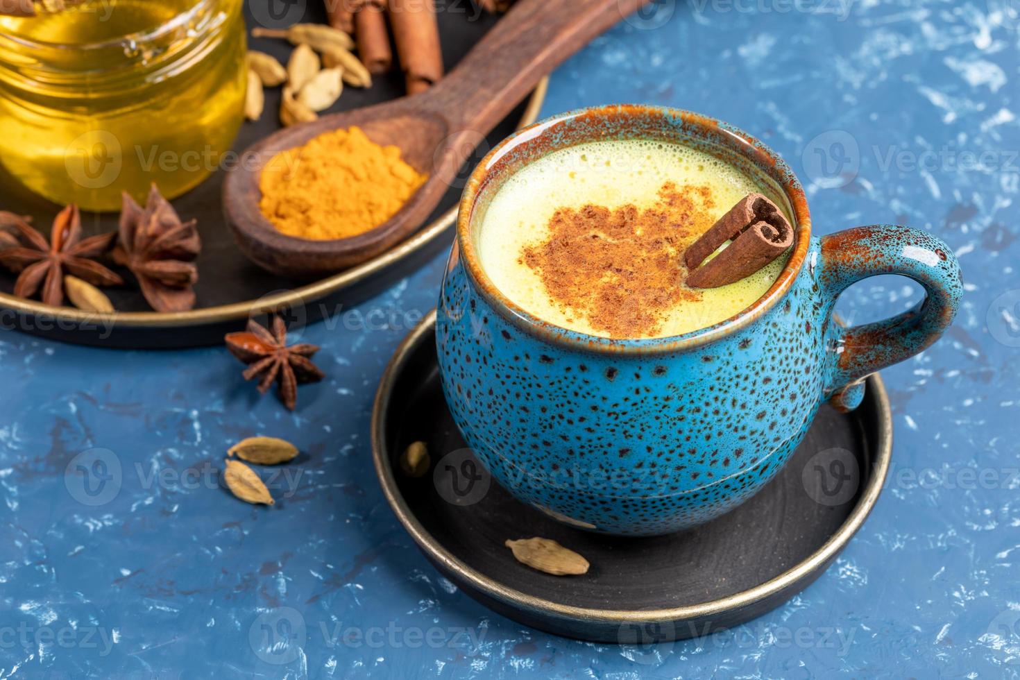 tasse bleue de lait de latte de curcuma doré traditionnel indien avec cardamome, anis, miel et bâton de cannelle sur bleu. photo