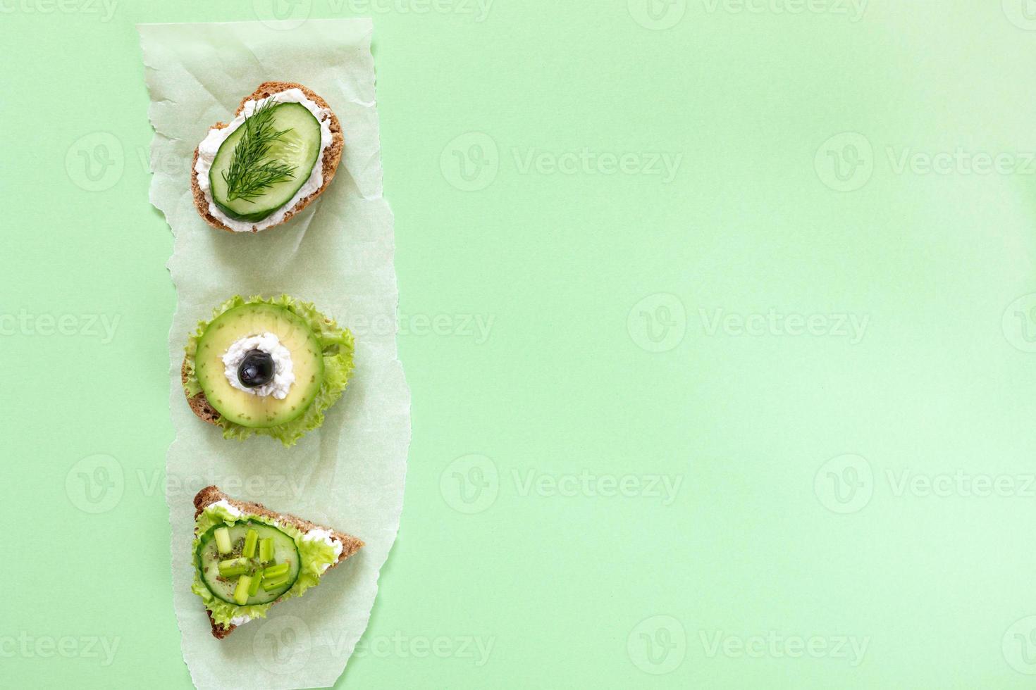 trois sandwichs végétariens sur un morceau de papier parchemin sur fond vert. photo