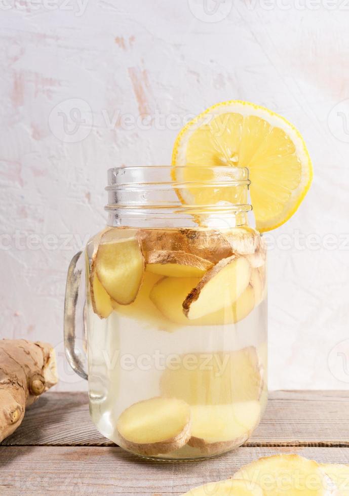 gros bocal en verre avec de l'eau au gingembre et une tranche de citron sur une table en bois. photo