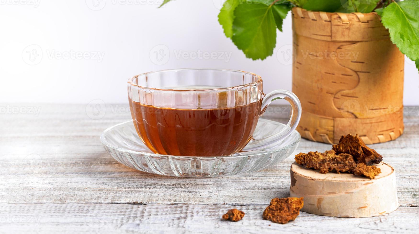 infusion curative de chaga aux champignons de bouleau dans une tasse en verre, morceaux de chaga sur une table en bois en gros plan avec espace de copie. photo