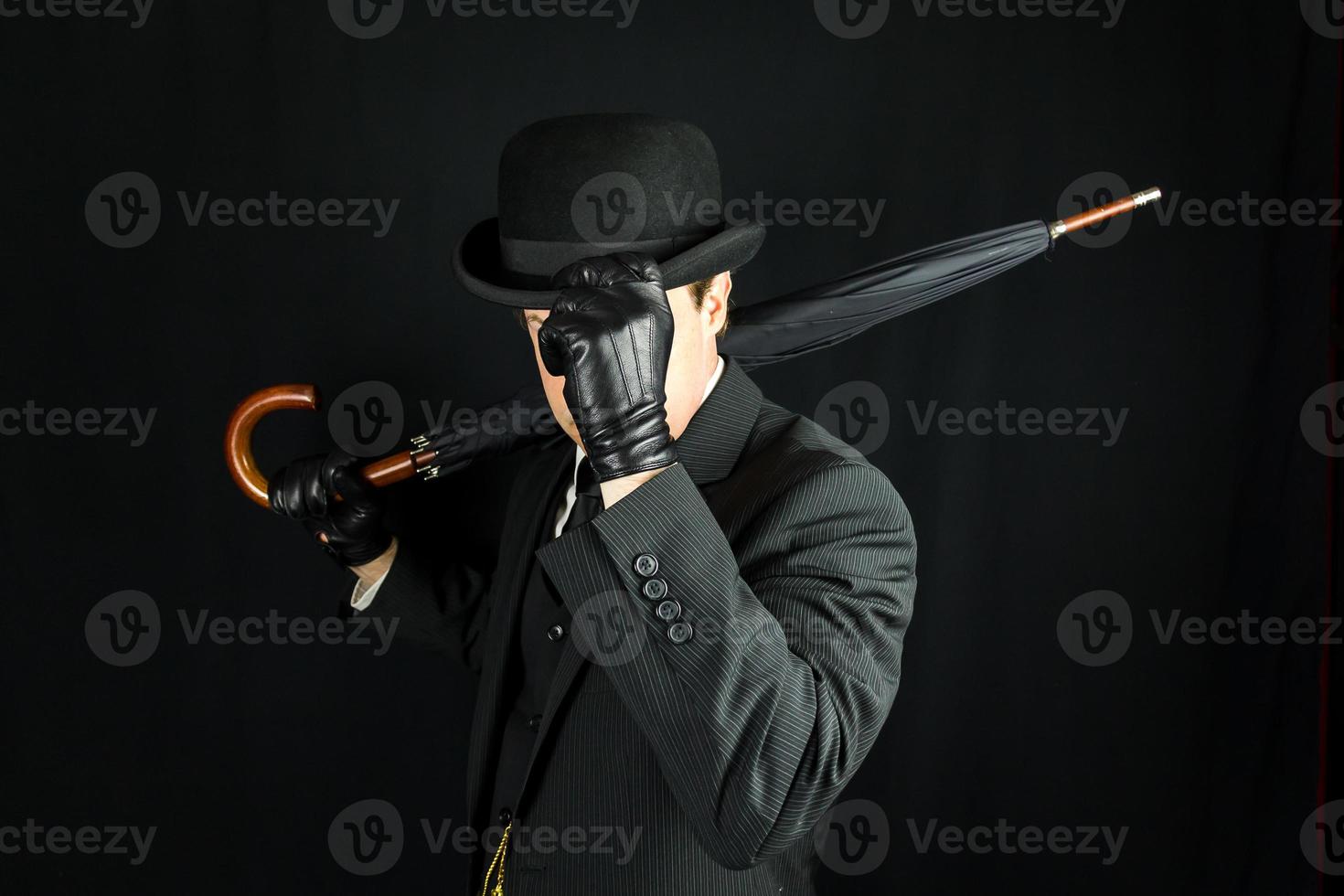 gentleman en costume sombre basculant chapeau melon sur fond noir. concept de gentleman britannique classique et excentrique photo