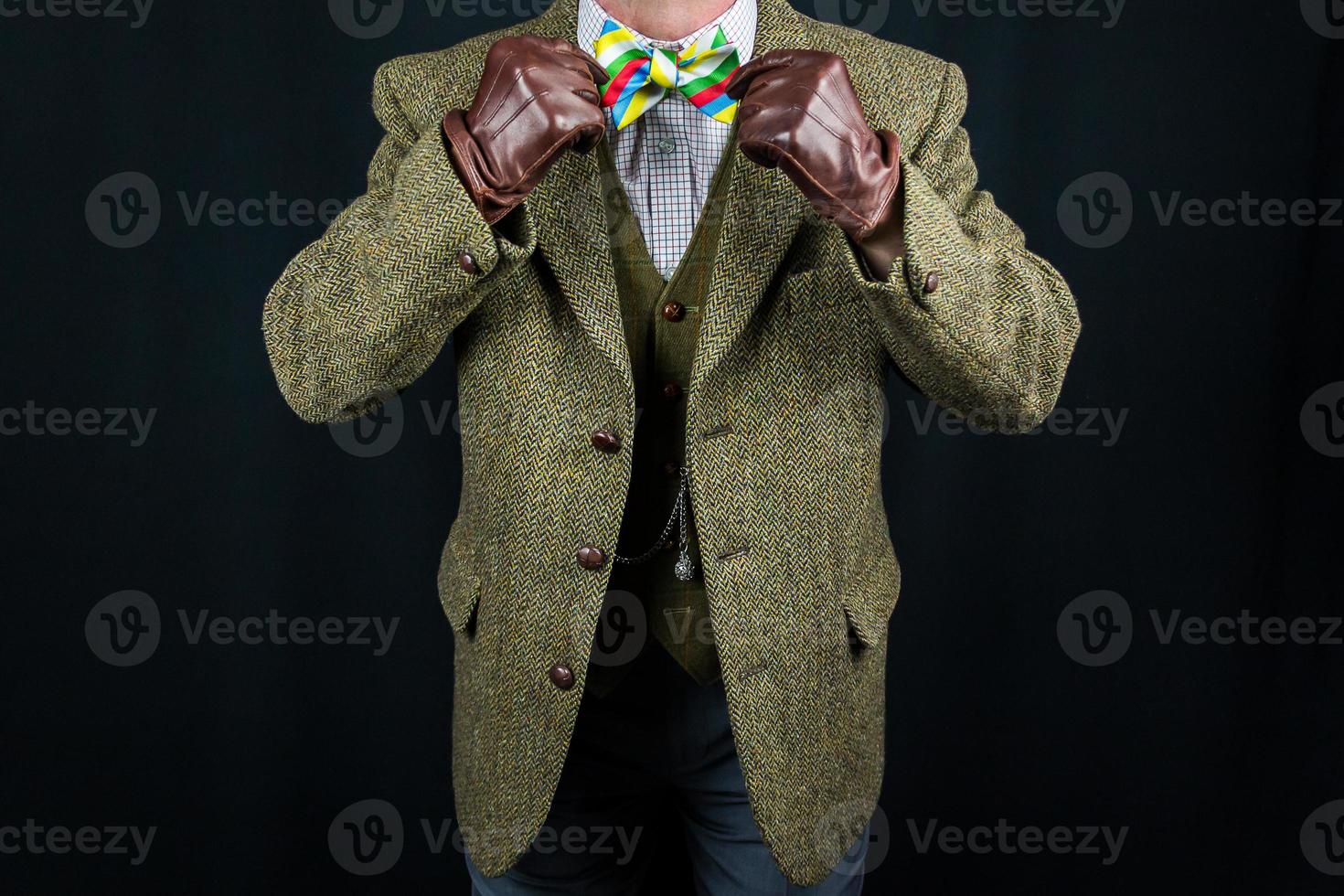 gentleman en costume de tweed et gants en cuir redressant le noeud papillon sur fond noir. concept de gentleman britannique classique et excentrique photo