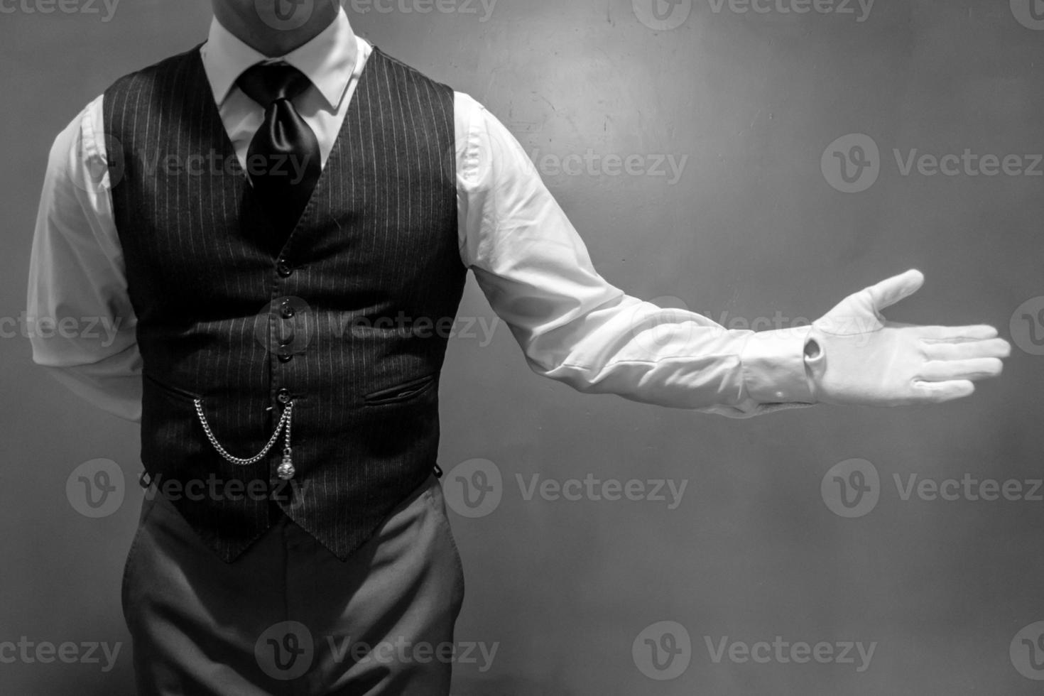 portrait noir et blanc d'un majordome bien habillé portant des gants blancs avec un geste de bienvenue. concept de l'industrie des services et de l'hospitalité professionnelle photo