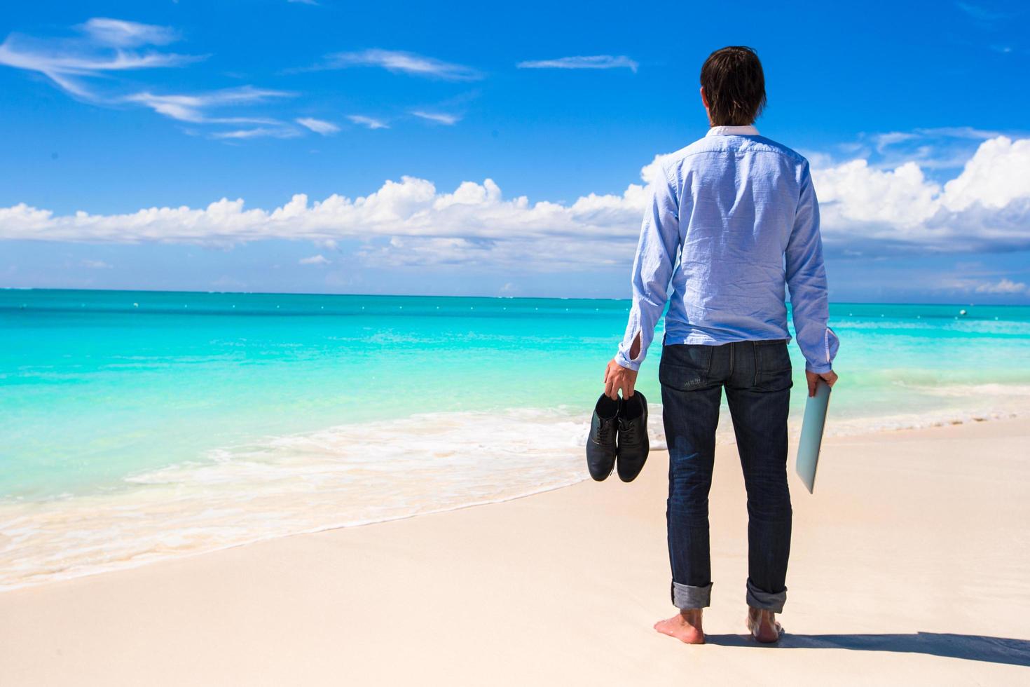 homme avec ordinateur portable et chaussures à la plage photo