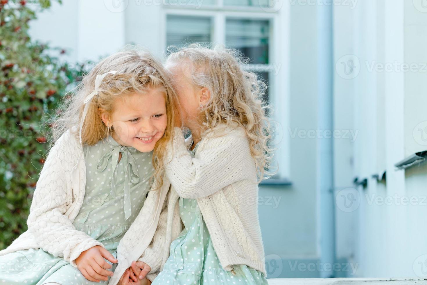 deux petites filles mignonnes sont assises dans le jardin et partagent des secrets. une fille chuchote quelque chose à l'oreille d'une autre. les deux sœurs ont une relation étroite. photo