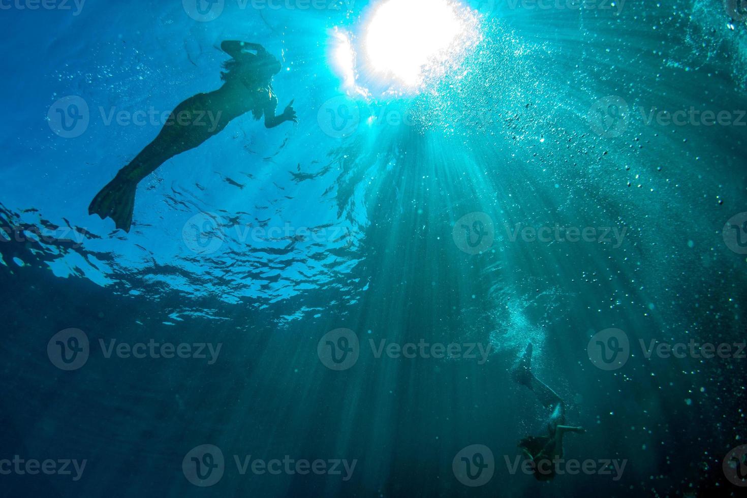 deux sirènes nageant sous l'eau dans la mer d'un bleu profond photo