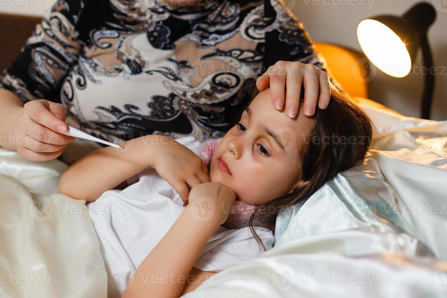 jeune mère vérifiant la température de sa fille malade au lit photo