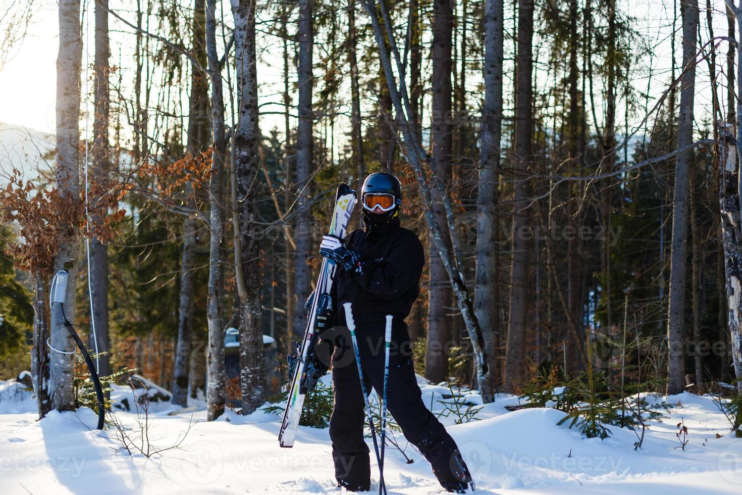 skieur prêt à tenir du matériel de ski avec rétro-éclairage solaire sur la piste de ski - jeune athlète dans les montagnes enneigées pour les vacances d'hiver - concept de sport et concept de vacances - se concentrer sur son visage - filtre chaud photo