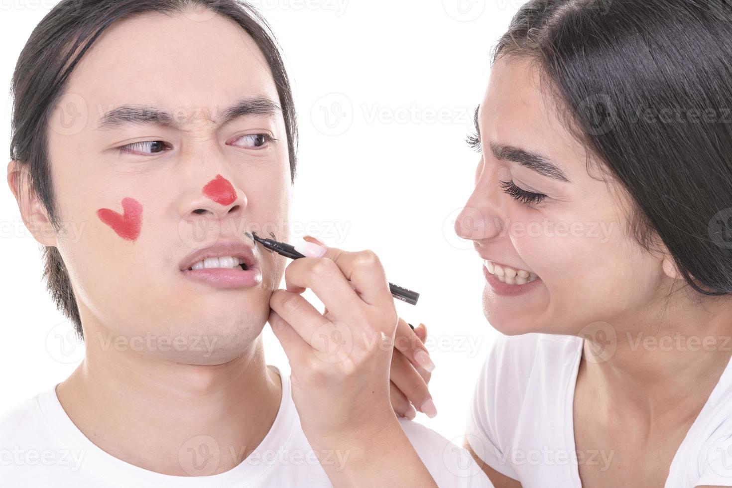 couple mixte s'amusant. modèle féminin arabe et modèle masculin asiatique qui ont noyé des moustaches et un cœur sur son visage. isolé sur fond blanc. photo