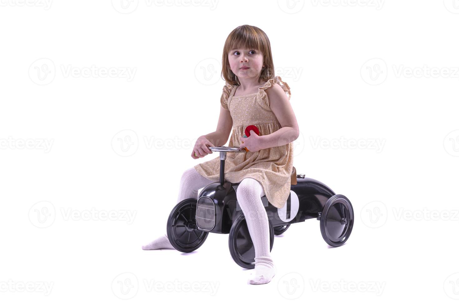 petite fille chevauchant une petite voiture de style rétro. fille chevauchant une vieille voiture à pédales en métal pour enfants du XIXe siècle. photo