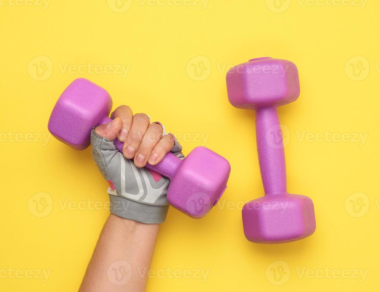 la main féminine dans un gant de sport rose tient un haltère violet d'un kilogramme photo