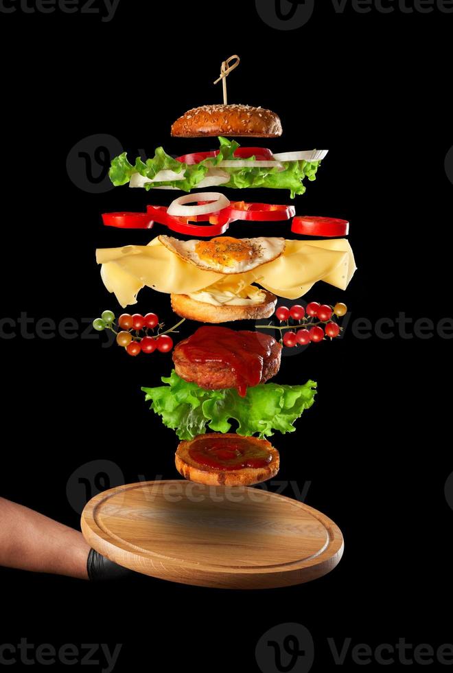 planche de bois ronde et couches d'un grand cheeseburger flottant dans l'air photo