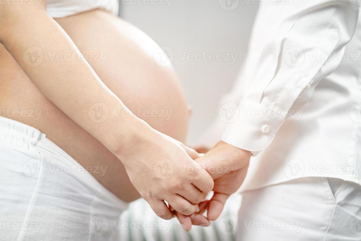 femme enceinte et son épissure de main de mari étreignant le ventre en forme de coeur montrent l'amour pour le bébé à naître dans le ventre se détendre à la maison dans la chambre. attendre la date de naissance attend un bébé debout à l'extérieur photo