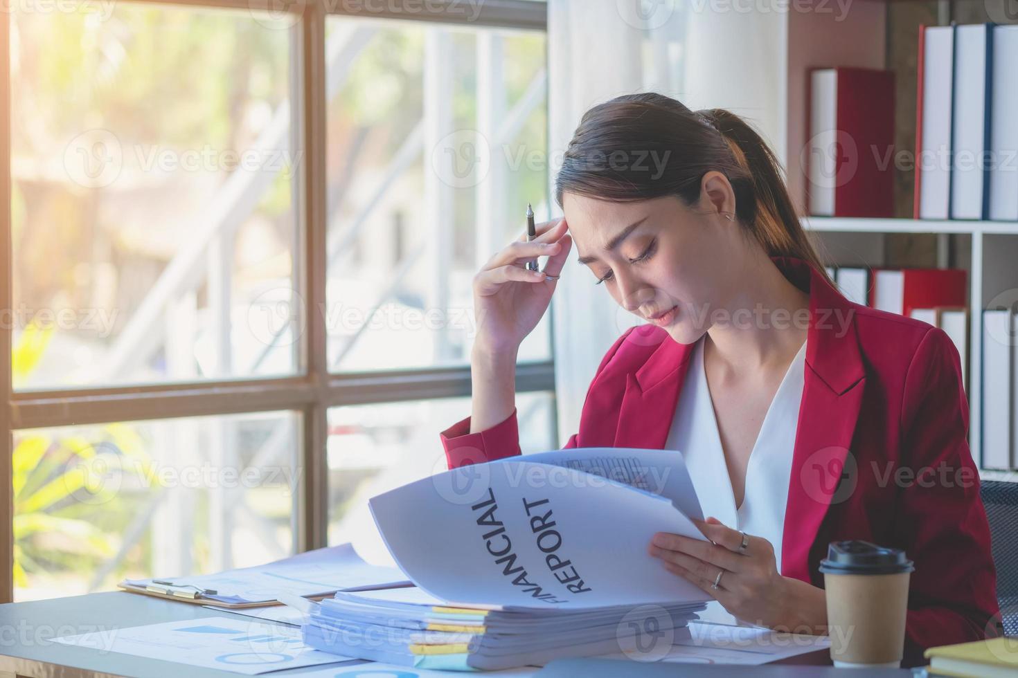 financier, femme d'affaires asiatique en costume rouge tenant une tasse de café assis sur le bureau au bureau, ayant un ordinateur pour faire du travail comptable sur le lieu de travail pour calculer le bénéfice annuel par devoir, idée d'entreprise photo