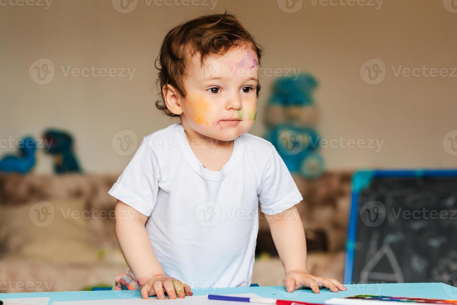 un petit garçon dessine avec des marqueurs colorés sur une feuille de papier photo