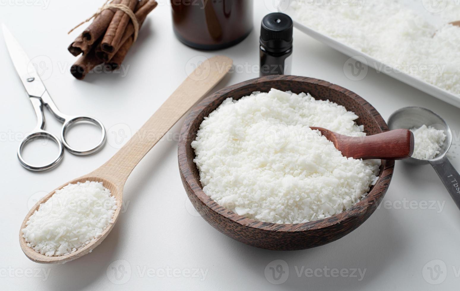 ingrédients pour la fabrication de bougies, flocons de cire de soja, bougies, mèches de cannelle et cuillères en bois sur fond de marbre clair photo