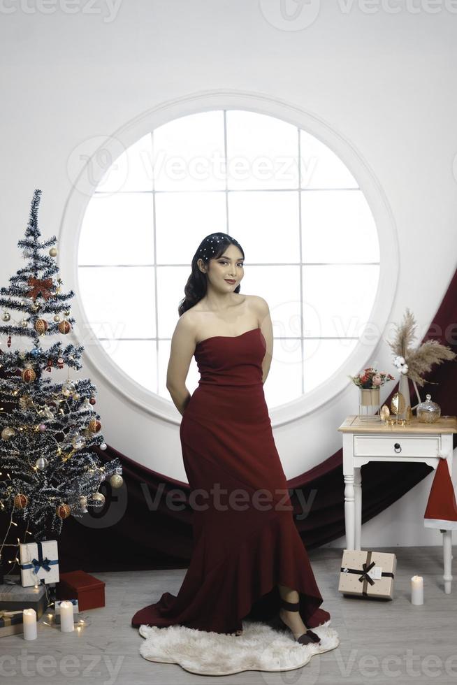 portrait d'une jolie jeune fille vêtue d'une robe rouge, souriant à la caméra, debout dans un salon de noël décoré à l'intérieur photo