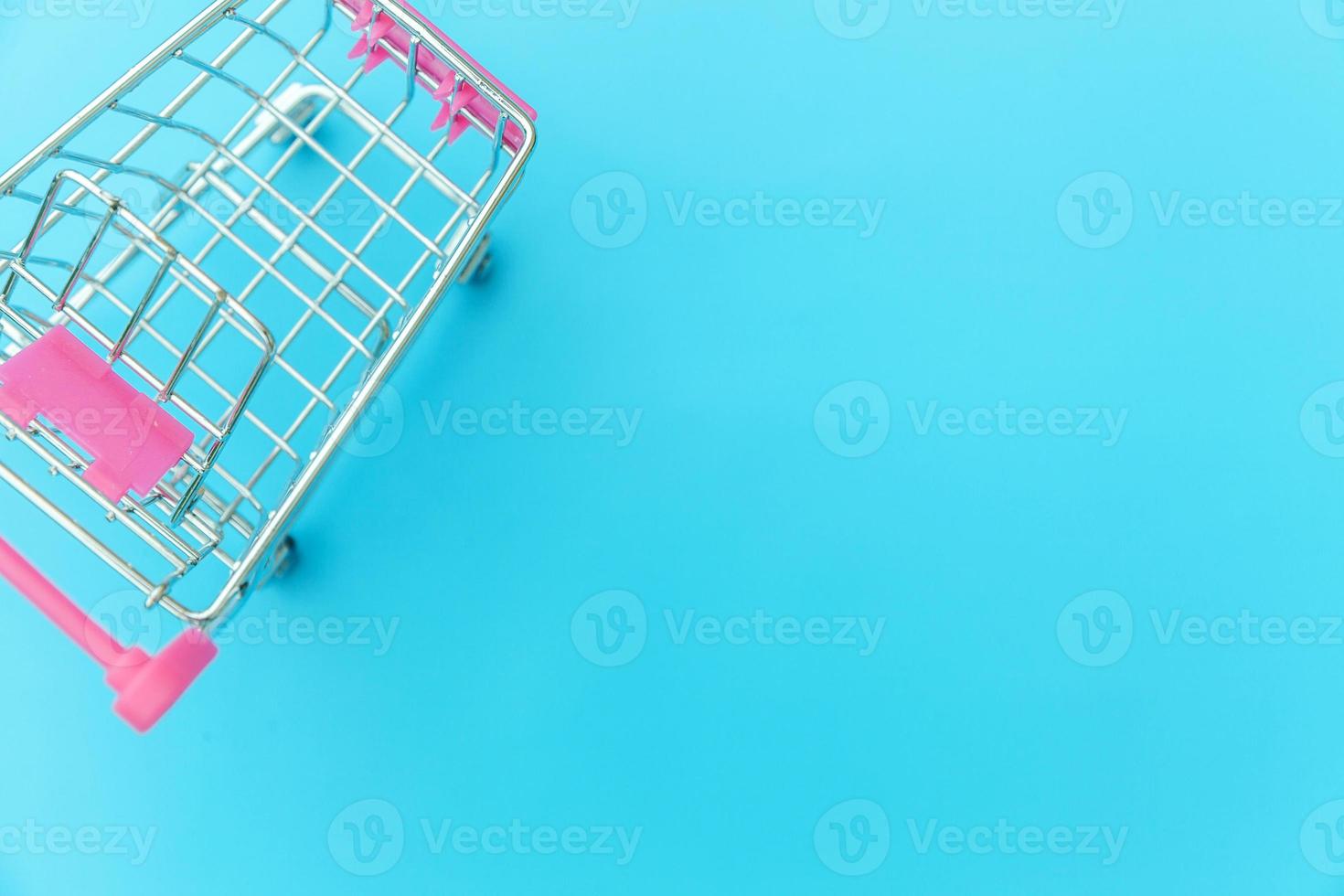 petit chariot d'épicerie de supermarché pour faire du shopping jouet avec roues isolées sur l'espace de copie de fond tendance coloré pastel bleu. vente acheter concept de consommateur de magasin de marché de centre commercial. photo