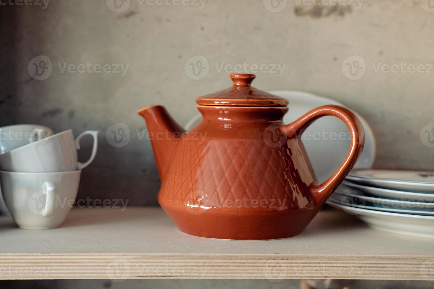 théière en argile brune sur une étagère blanche avec tasses et assiettes photo