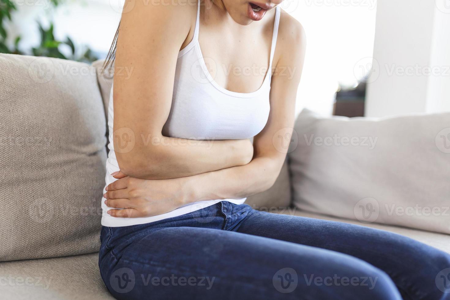 femme allongée sur un canapé qui a l'air malade dans le salon. belle jeune femme allongée sur le lit et se tenant la main sur le ventre. femme ayant des maux d'estomac douloureux au lit, période menstruelle photo