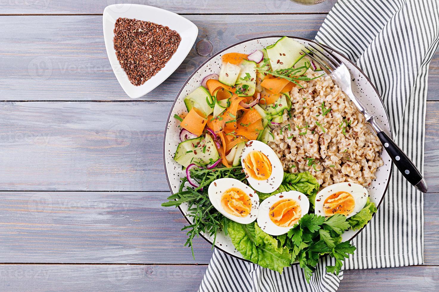 bol de petit déjeuner avec flocons d'avoine, courgettes, laitue, carotte et œuf à la coque. salade fraiche. la nourriture saine. bol bouddha végétarien. vue de dessus photo