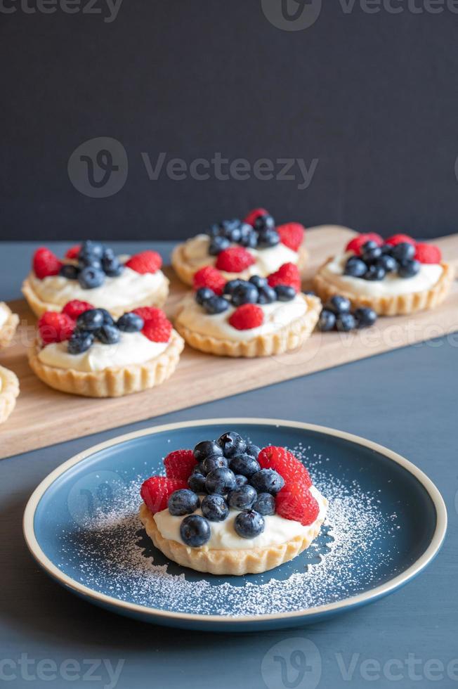 Assortiment de tartes aux framboises et myrtilles sur une table bleue devant un fond gris. photo