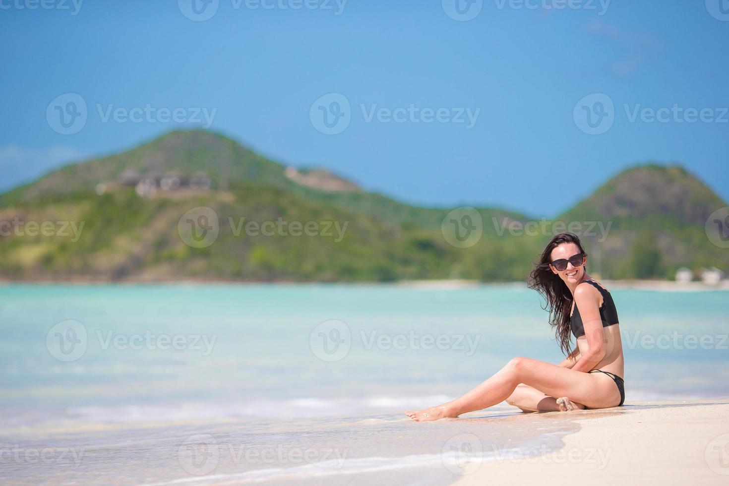 femme assise sur la plage en riant et en profitant des vacances d'été en regardant la caméra. beau modèle en bikini assis. photo