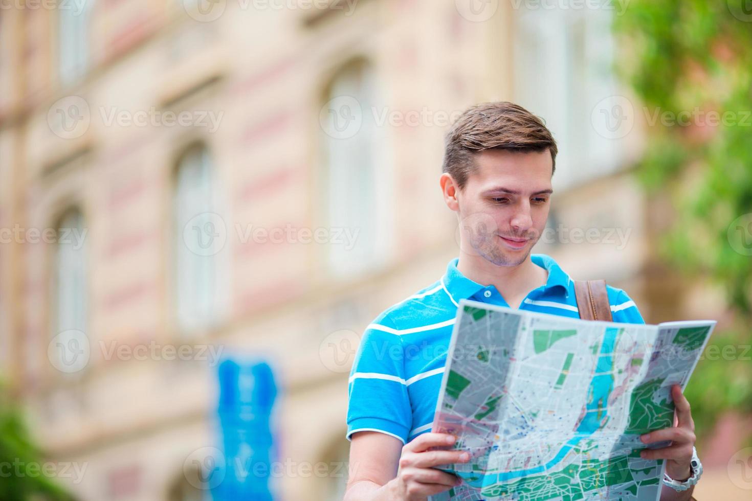 jeune homme à lunettes de soleil avec un plan de la ville et un sac à dos en europe. touriste caucasien regardant la carte de la ville européenne à la recherche d'attractions. photo