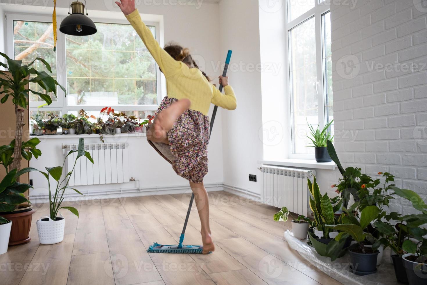 une fille danse avec une vadrouille pour nettoyer le sol dans une nouvelle maison - nettoyage général dans une pièce vide, la joie de déménager, aide aux tâches ménagères photo
