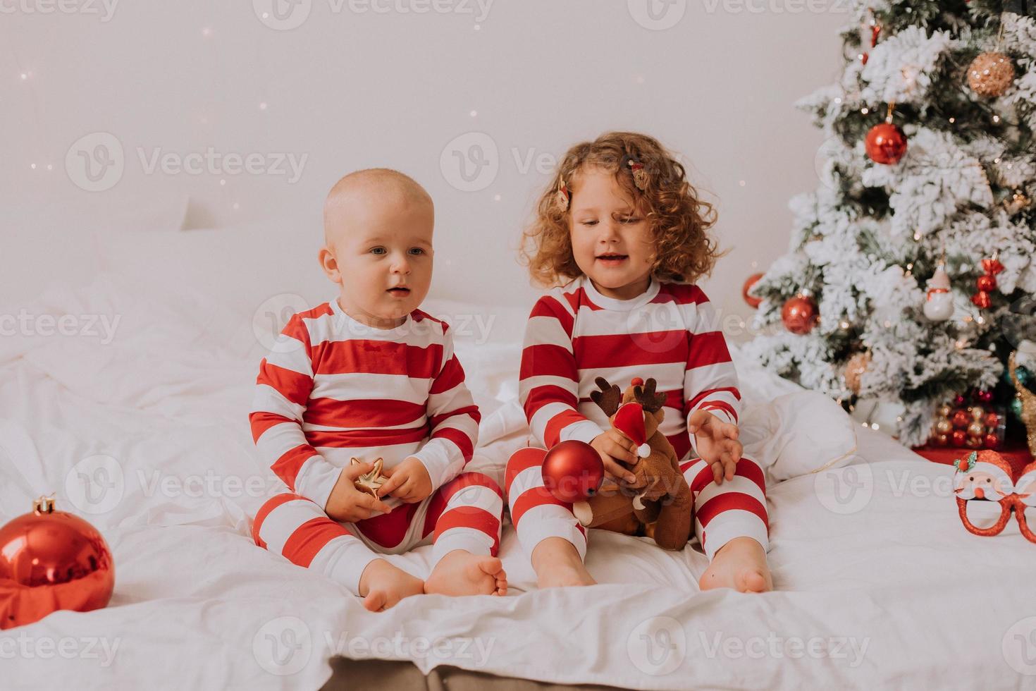 les enfants en pyjama rouge et blanc mangent des bonbons de noël assis dans leur lit. frère et sœur, garçon et fille partagent des cadeaux. Matin de noël. mode de vie. espace pour le texte. photo de haute qualité