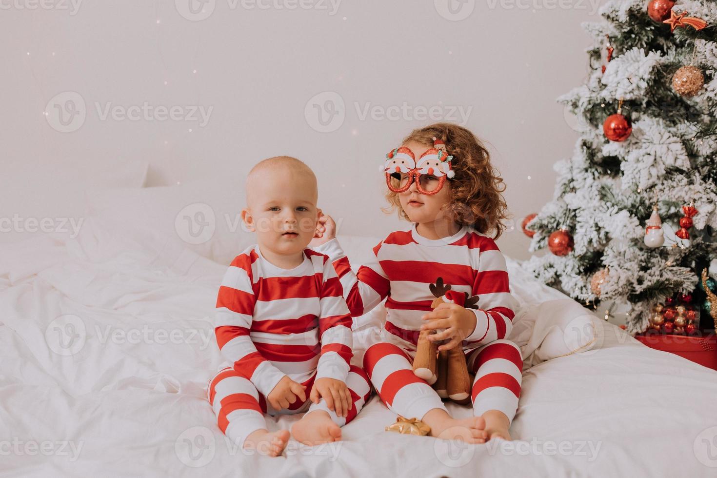 les enfants en pyjama rouge et blanc mangent des bonbons de noël assis dans leur lit. frère et sœur, garçon et fille partagent des cadeaux. Matin de noël. mode de vie. espace pour le texte. photo de haute qualité