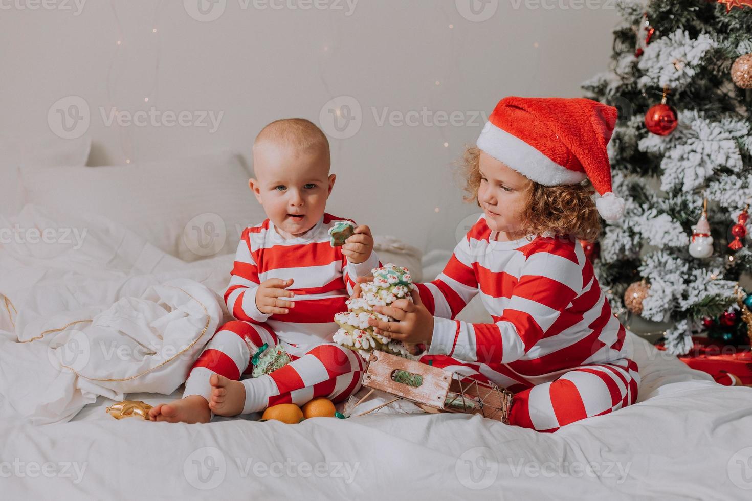 les enfants en pyjama rouge et blanc mangent des bonbons de noël assis dans leur lit. frère et sœur, garçon et fille partagent des cadeaux. Matin de noël. mode de vie. espace pour le texte. photo de haute qualité