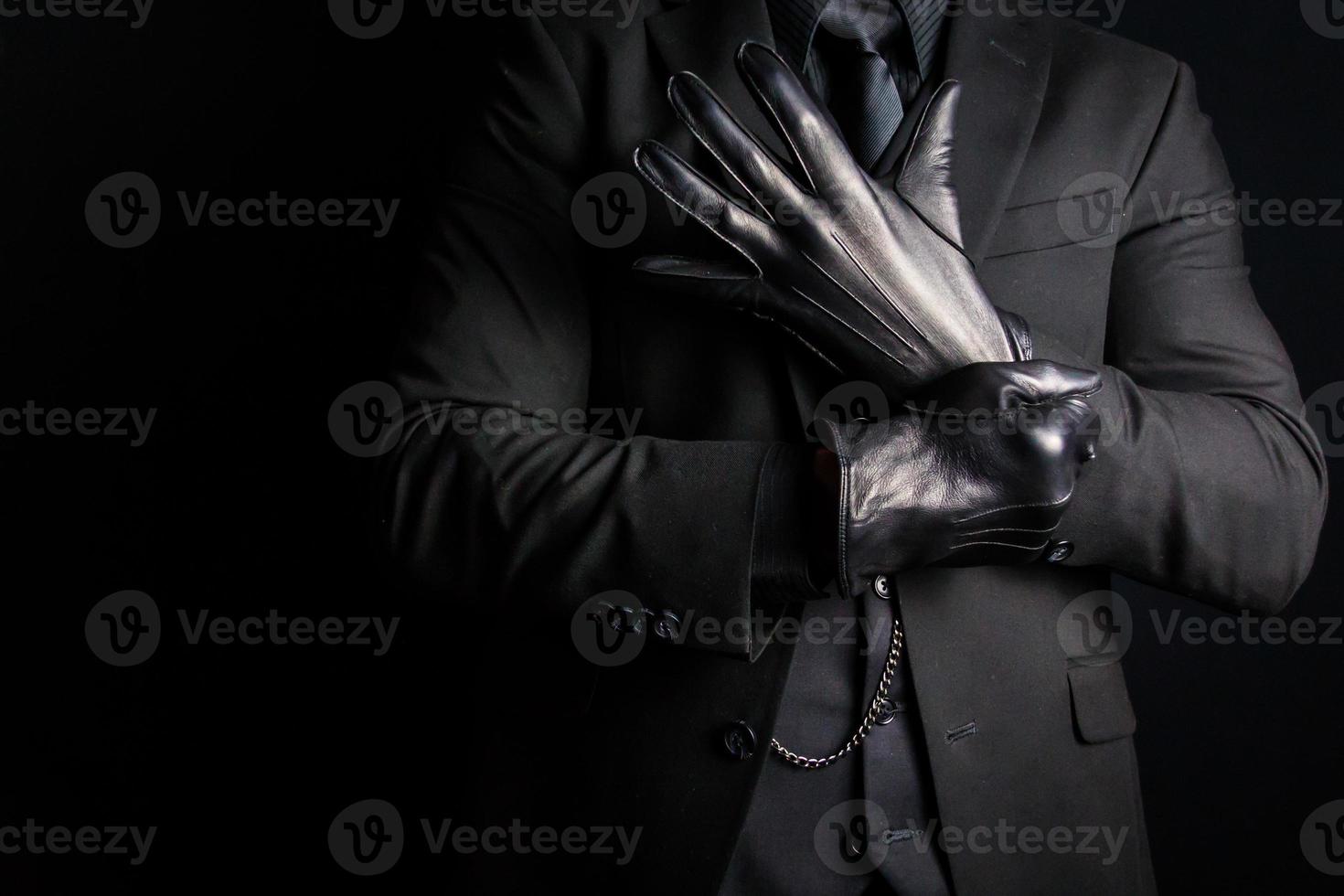 portrait d'un homme fort en costume sombre tirant sur des gants en cuir noir. sombre activité criminelle. menace de violence dangereuse photo